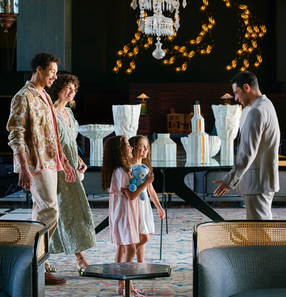 Vestíbulo elegante con lámpara central, mobiliario contemporáneo y una familia conversando con el personal.