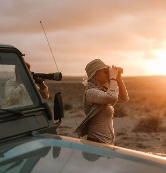 Personne observant les oiseaux avec des jumelles près d’un 4x4 au coucher du soleil aux îles Canaries.