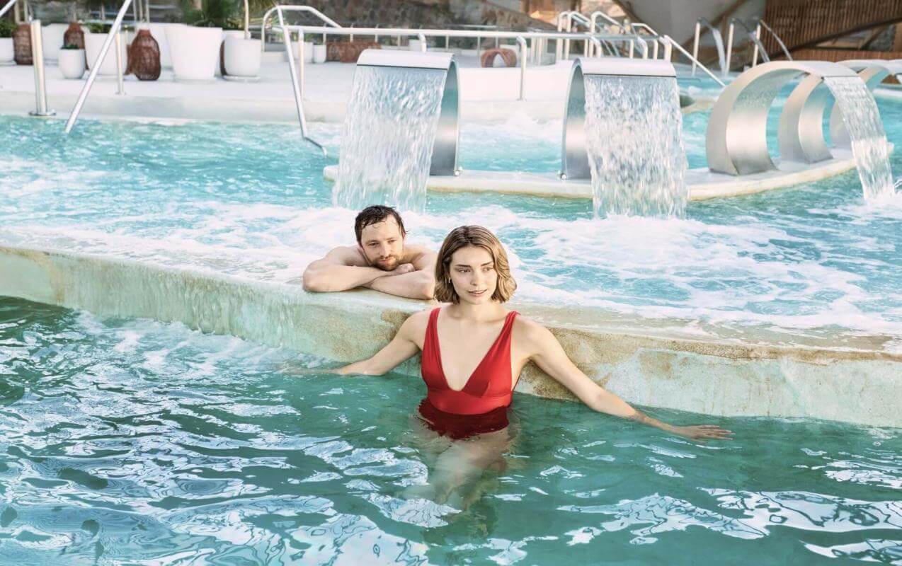 Couple en train de profiter de la piscine de thalassothérapie équipée de jets et de cascades, dans un espace dédié au bien-être et à la détente.