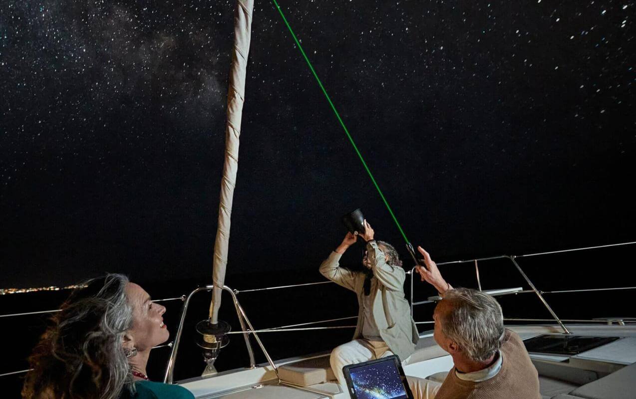 Observation astronomique depuis un voilier sous un ciel étoilé, avec un pointeur laser, sur les eaux calmes de l’océan.