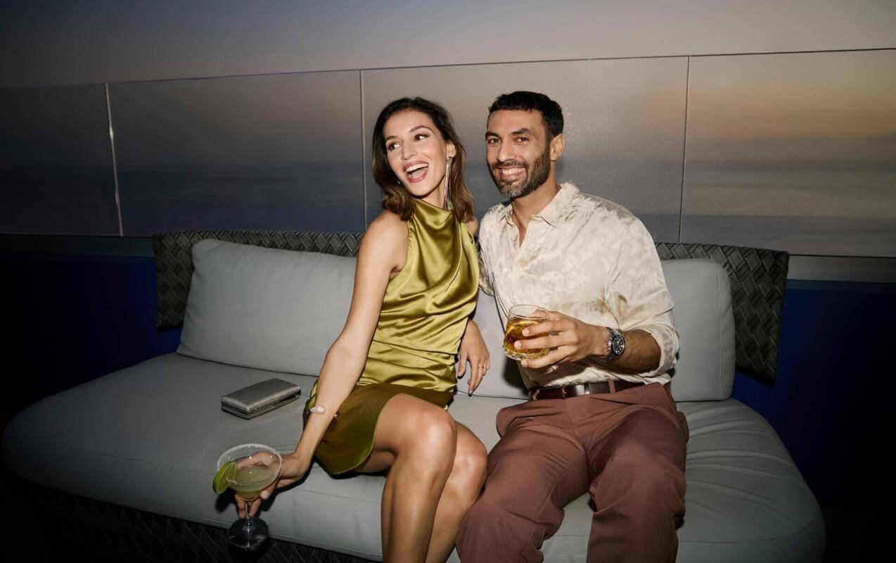 Couple en train de déguster des cocktails sur une terrasse au coucher du soleil, avec vue sur la mer et dans une atmosphère élégante.