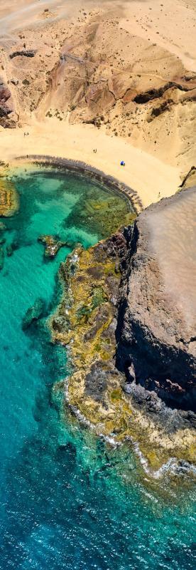 Vue de la plage du Papagayo à Lanzarote, avec son sable doré, ses falaises volcaniques et sa mer turquoise.