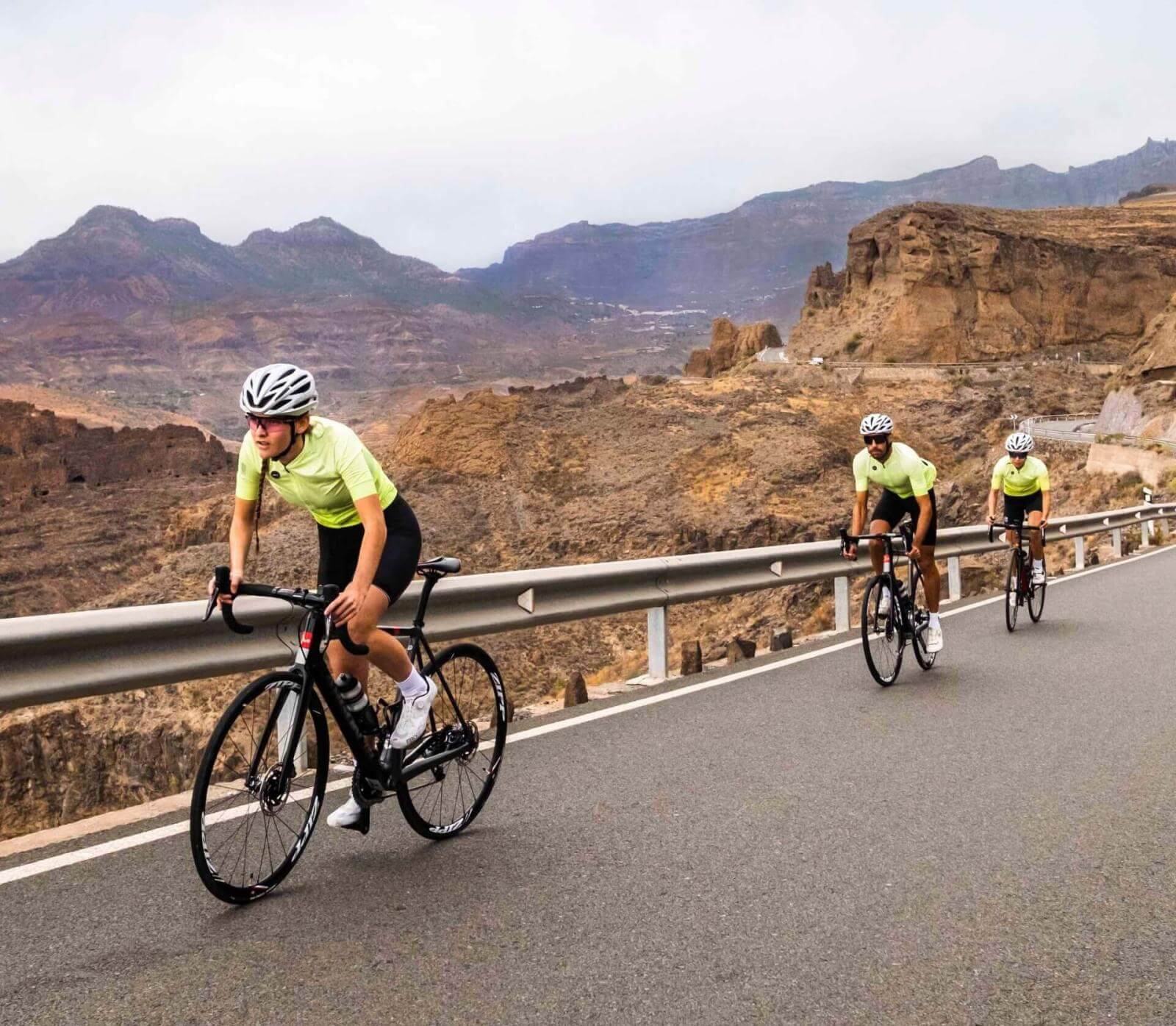 Trois cyclistes en train de s’entraîner sur une route bitumée au cœur d’un paysage montagneux.