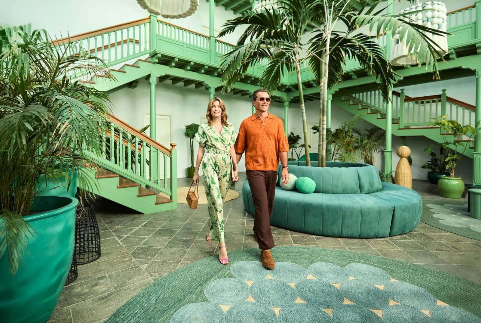 Couple en train de marcher dans un hall inspiré de l’architecture traditionnelle canarienne, baigné de lumière et orné de végétation tropicale.