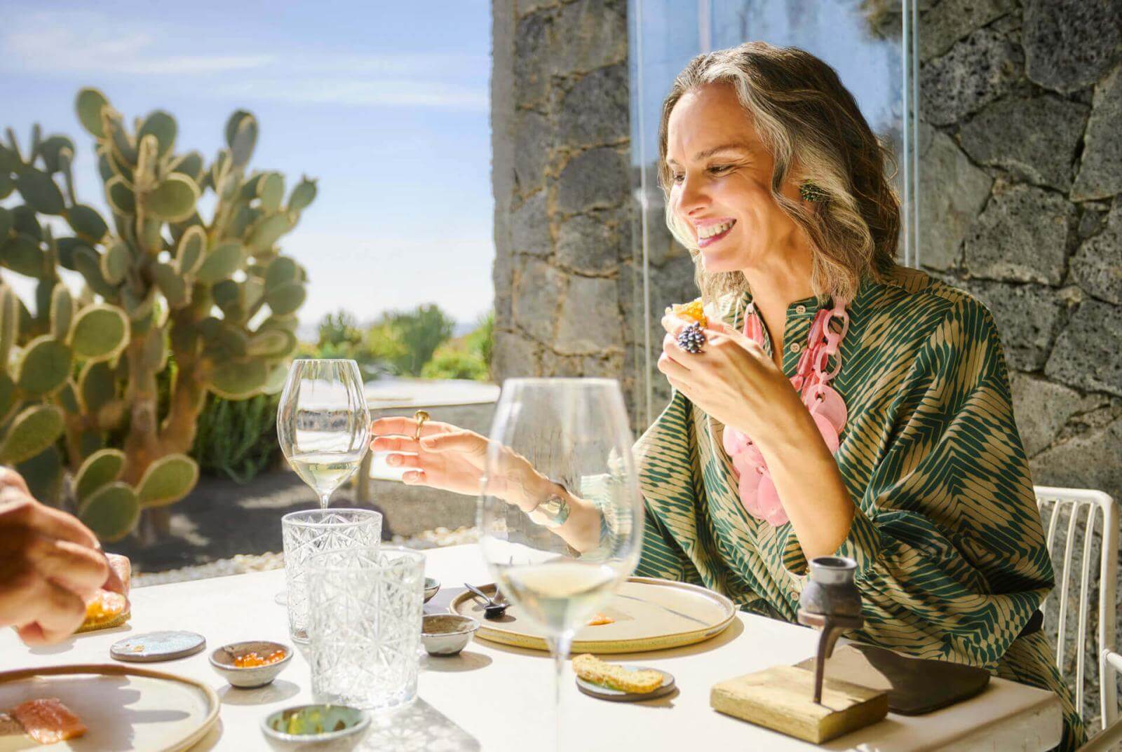 Personne en train de profiter d’un apéritif et d’un verre de vin à une table près d’une porte, avec des cactus en arrière-plan.