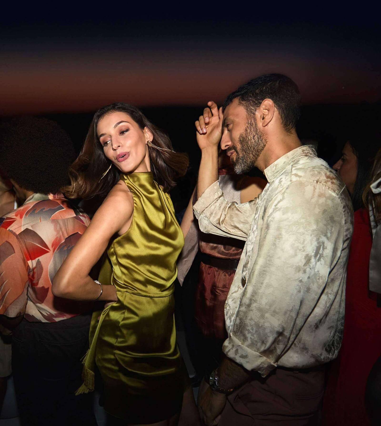 Couple en train de danser sur une terrasse rooftop avec vue sur la mer à la tombée de la nuit.