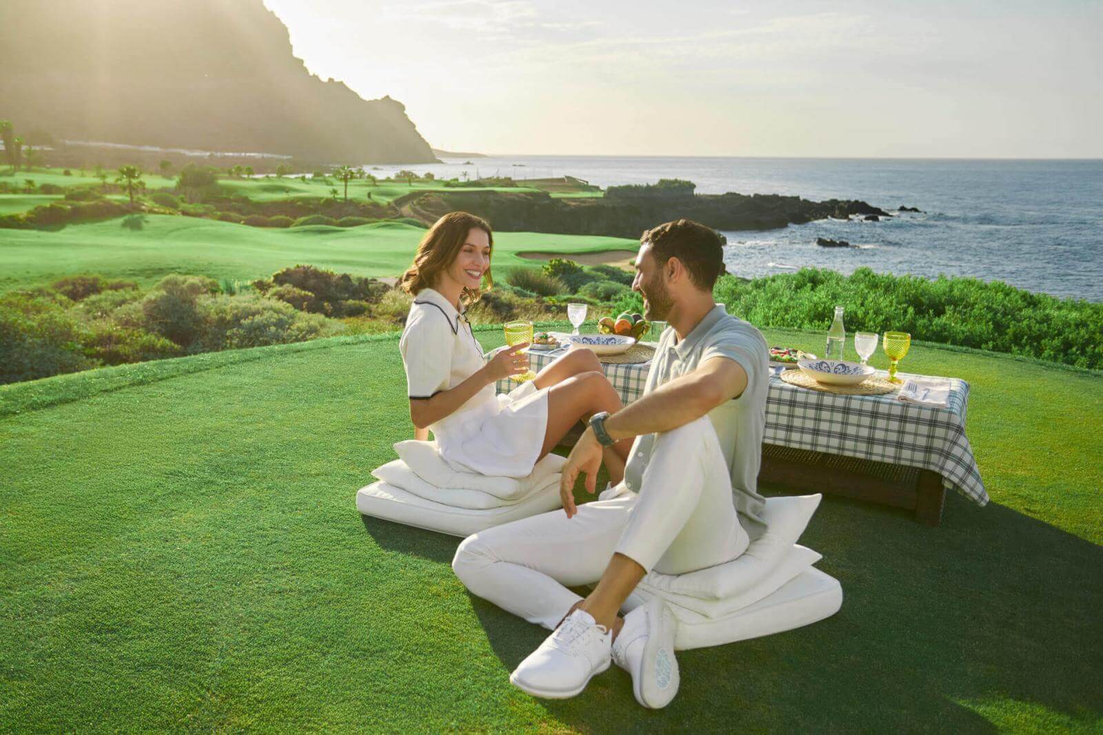 Couple en train de profiter d’un pique-nique avec une table bien fournie sur le parcours de golf face à l’océan et les montagnes dans les îles Canaries.