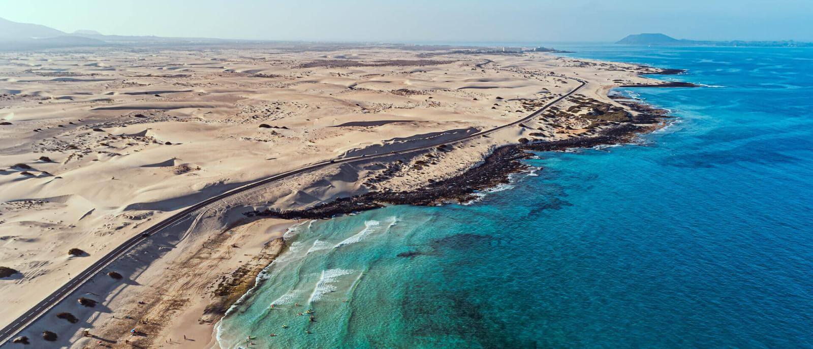 Vue aérienne des Dunes de Corralejo, avec de vastes étendues de sable baignées par une mer turquoise.