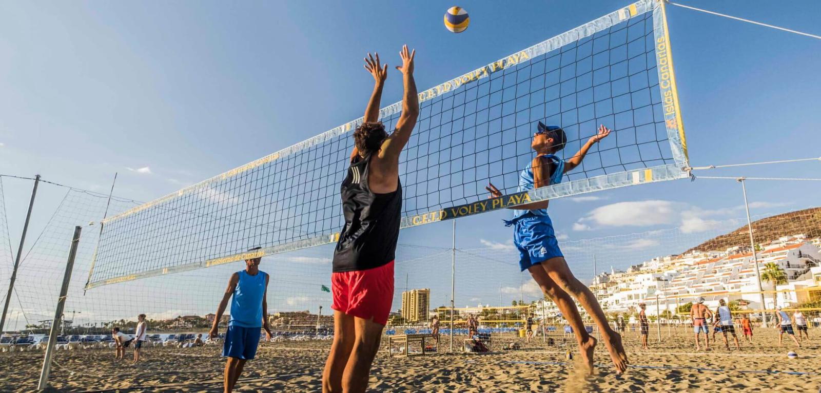 Personnes en train de jouer au beach-volley et de sauter pour récupérer le ballon.