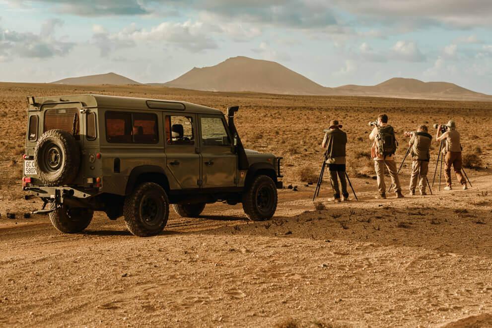 Personnes avec des appareils photo et des trépieds observant des oiseaux dans un paysage aride près d'un 4x4.