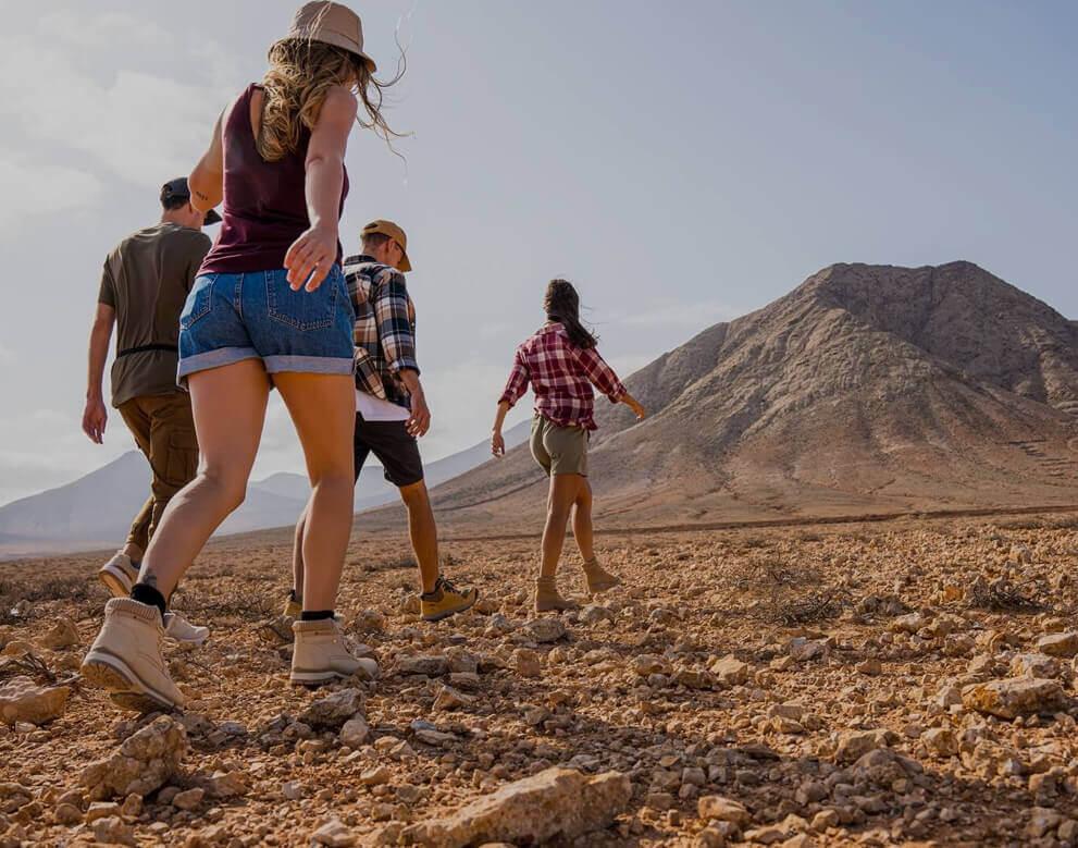 Groupe marchant sur un sol aride vers une montagne, dans un vaste paysage naturel.