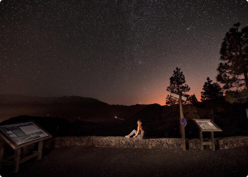 Nuit étoilée depuis le mirador Llano del Jable, à La Palma, avec des silhouettes de montagnes et une personne.