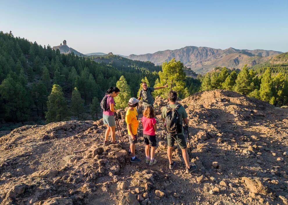 Excursion en groupe dans le Parc rural du Roque Nublo, avec sol rocheux, pinède canarienne et sommet au fond.