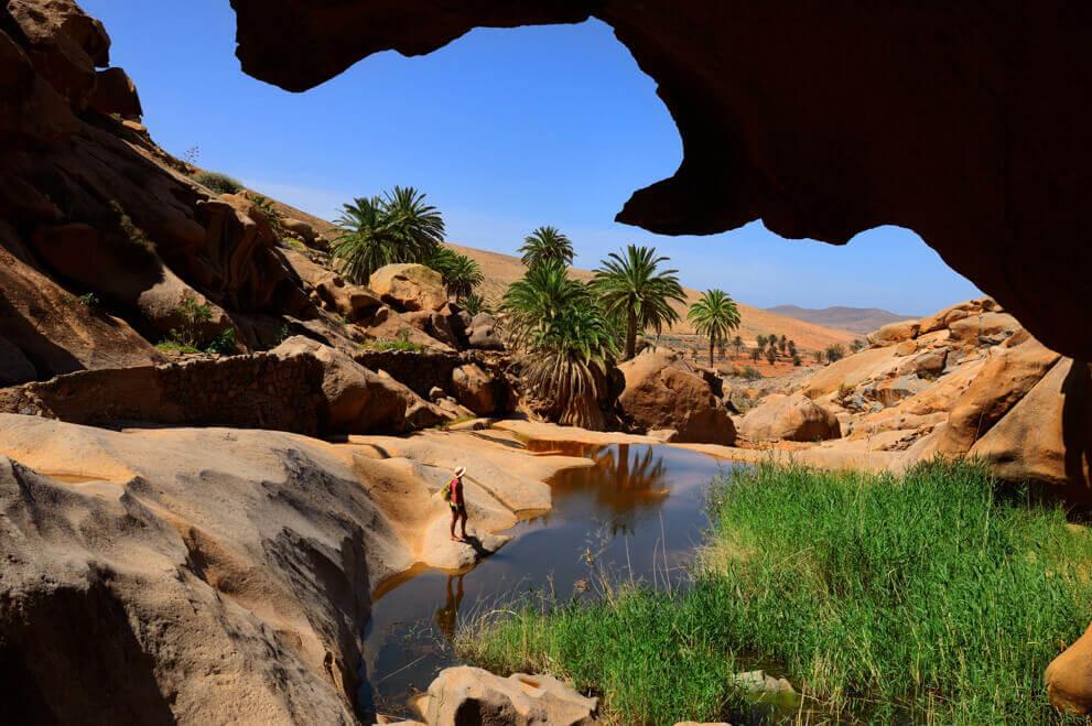 Ravin de Las Peñitas à Fuerteventura, avec rochers, palmiers et petit bassin au milieu d’un paysage aride.