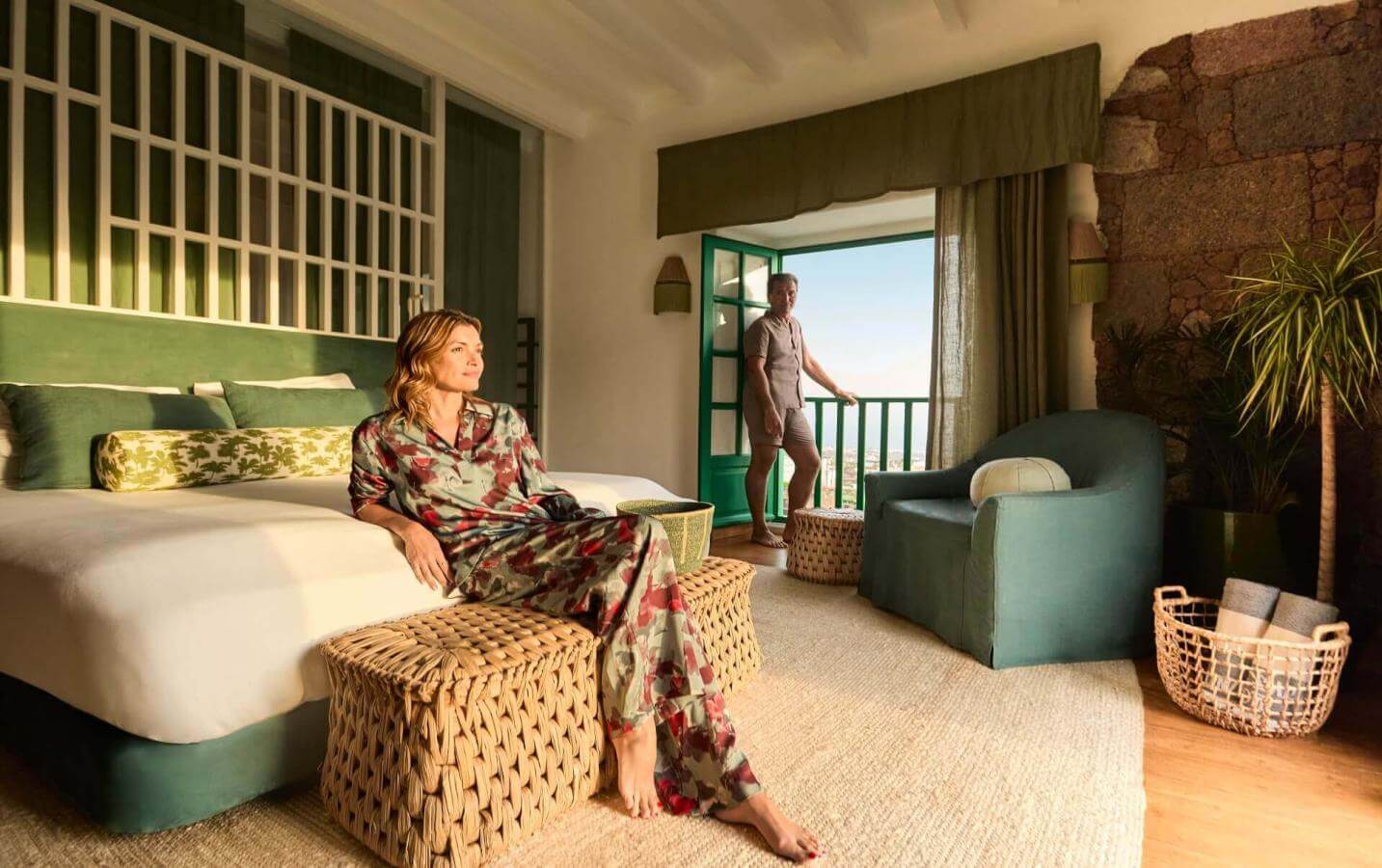 Personne détendue dans une chambre décorée dans des tons verts, avec une terrasse s’ouvrant sur le paysage, dans une ambiance chaleureuse et cosy.