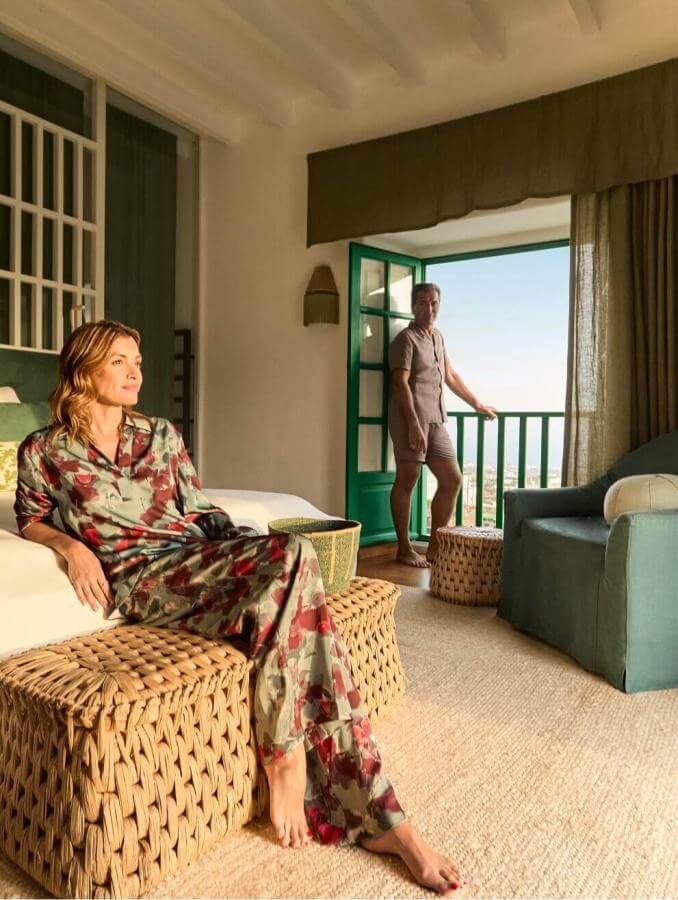 Personne détendue dans une chambre décorée dans des tons verts, avec une terrasse s’ouvrant sur le paysage, dans une ambiance chaleureuse et cosy.