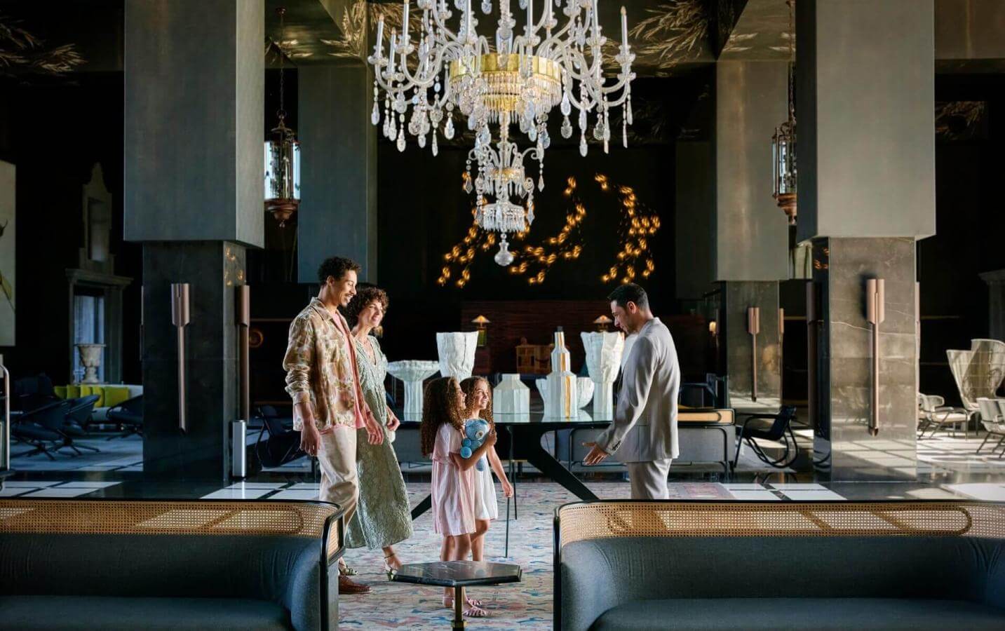 Famille à son arrivée dans un hôtel élégant avec des lustres en cristal et un mobilier sophistiqué, dans un grand espace ouvert au design contemporain.