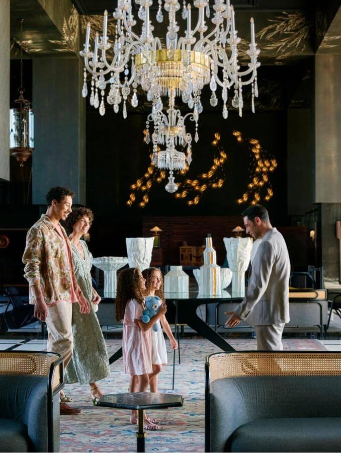 Famille à son arrivée dans un hôtel élégant avec des lustres en cristal et un mobilier sophistiqué, dans un grand espace ouvert au design contemporain.