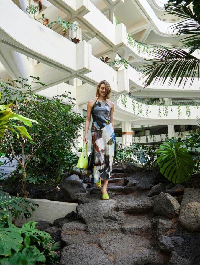 Personne en train de marcher sur un chemin bordé de végétation tropicale dans un intérieur à l’architecture blanche et au design organique.