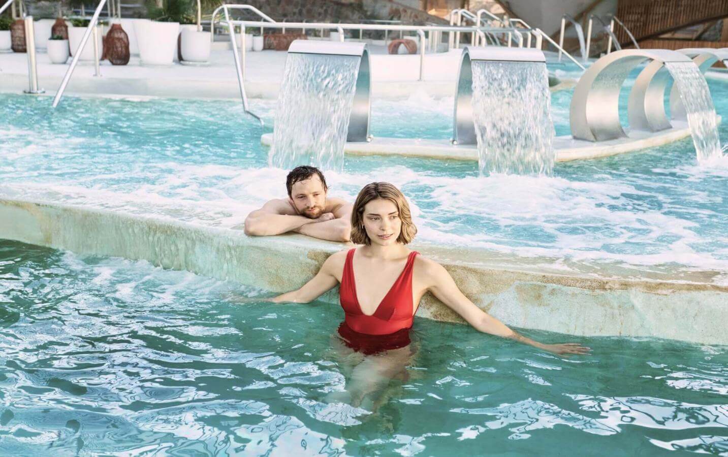 Couple en train de profiter de la piscine de thalassothérapie équipée de jets et de cascades, dans un espace dédié au bien-être et à la détente.
