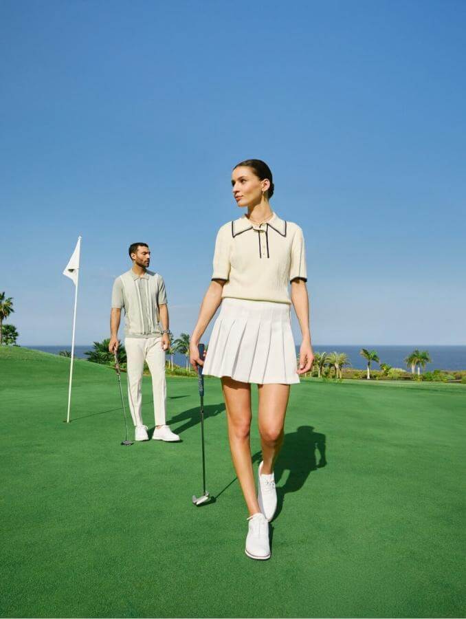 Personnes en train de jouer au golf sur un terrain vert au bord de la mer, avec un drapeau dans le trou et un ciel dégagé.
