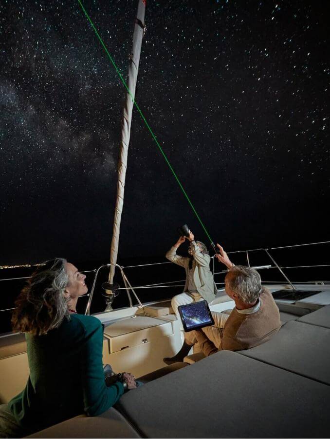 Observation astronomique depuis un voilier sous un ciel étoilé, avec un pointeur laser, sur les eaux calmes de l’océan.