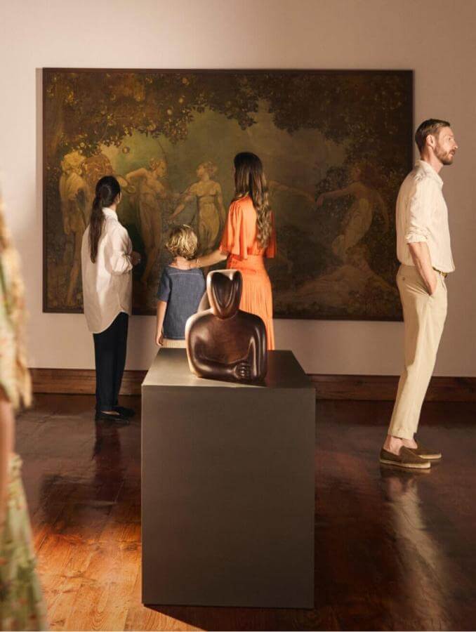 Groupe en train de visiter une exposition d’art dans un musée avec de grands tableaux et des sculptures dans une salle éclairée.