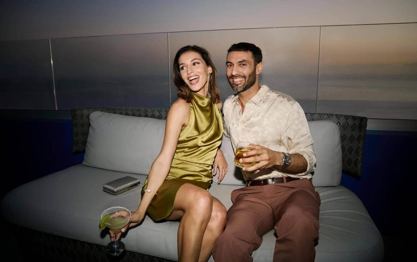 Couple en train de déguster des cocktails sur une terrasse au coucher du soleil, avec vue sur la mer et dans une atmosphère élégante.