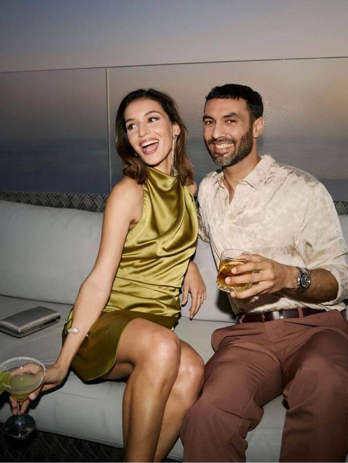 Couple en train de déguster des cocktails sur une terrasse au coucher du soleil, avec vue sur la mer et dans une atmosphère élégante.